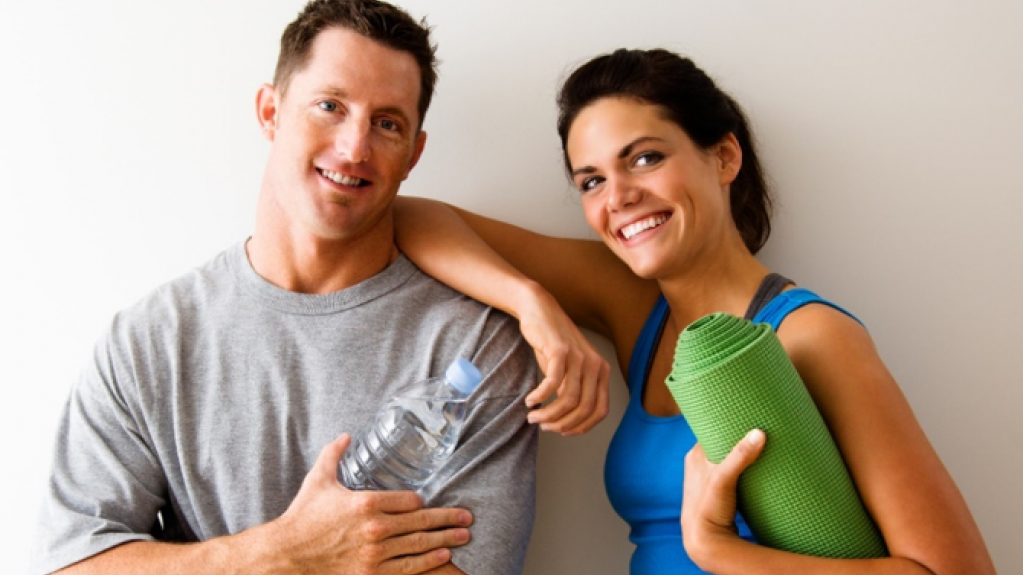 Was ist EMS Training? | StimaWELL EMS Sportliche Frau und Mann stehen an einer Wand und lächeln